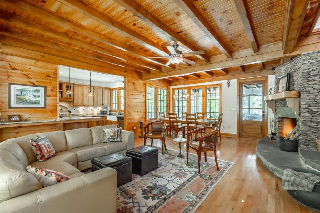 Lane's End great room with a cream sectional, dining table and stone fireplace under log beams on Lookout Mountain, Georgia