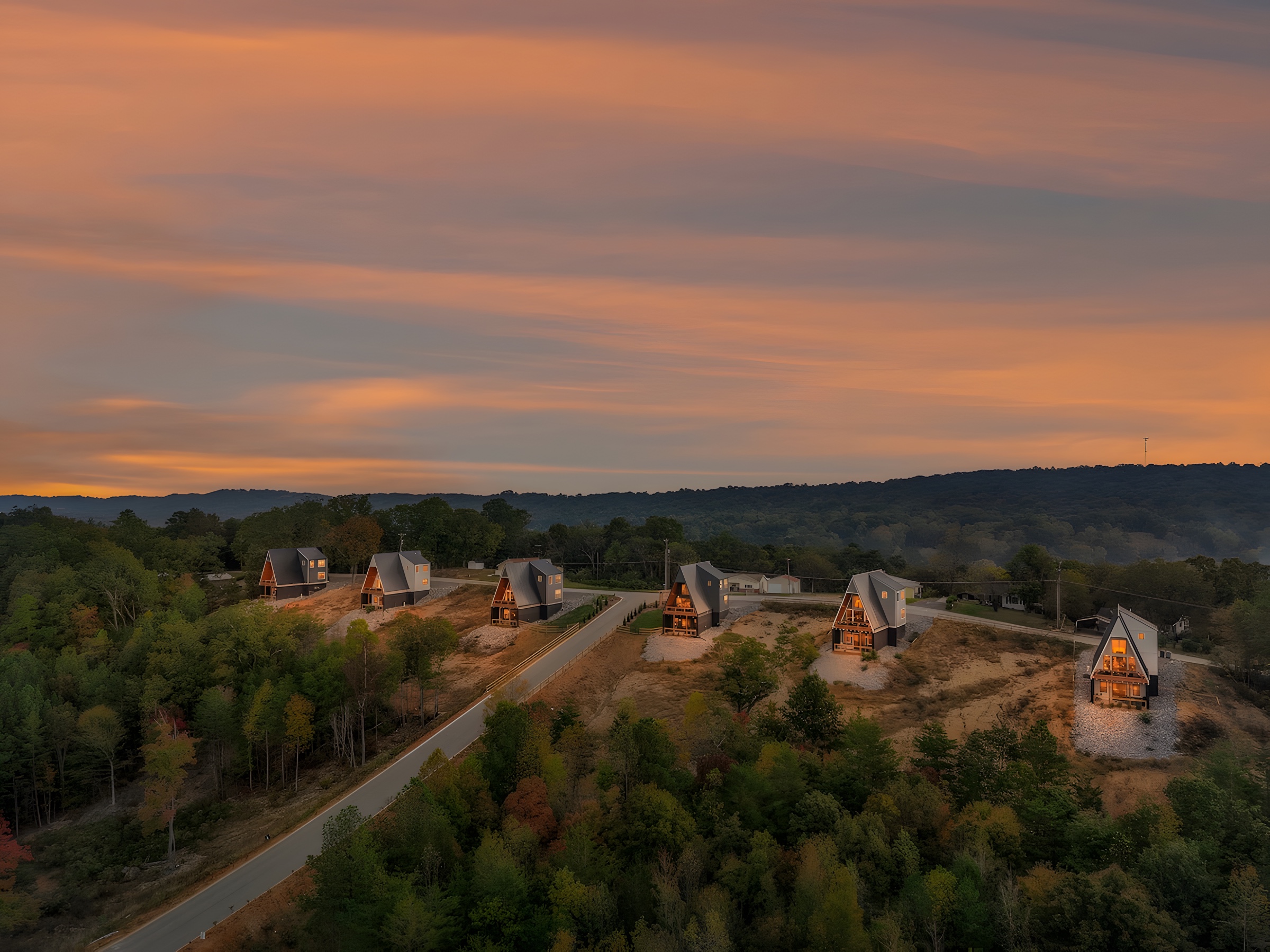 The six Alpine A-Frames cabins from the air at sunset, lit along a ridge road with a mountain ridge beyond, in Rossville, Georgia
