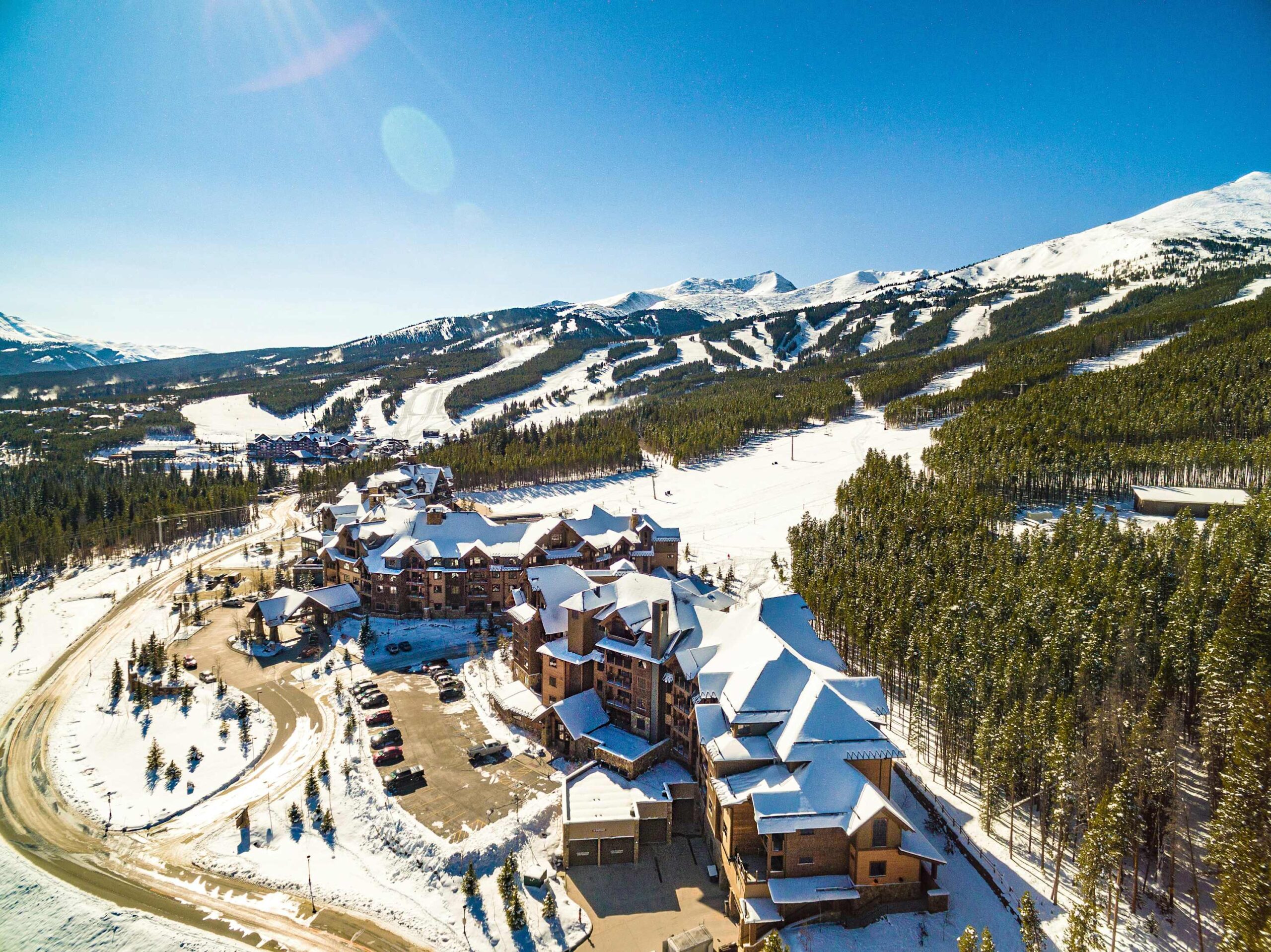 An aerial view of The Buffalo Lodge in snow, with ski slopes and peaks behind, in Silverthorne, Colorado